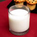 An Anchor Hocking tumbler of milk with muffins on a table.