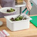 A woman using tongs to serve salad from a Carlisle white food pan.