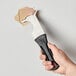 A hand holding a black plastic Allway Tools painter's multi-tool scraping paint from a wall.
