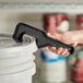 A hand with a black Allway Tools Plastic Pail Opener opening a white pail.