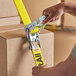A person using a Lift-All yellow polyester tie-down strap with U-hook to secure a box.