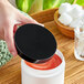 A hand holding a black 89/400 Smooth Lid over a white container with red liquid.