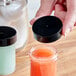 A hand holding a 38/400 black lid over a jar of orange liquid.