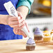 A person using an Ateco pastry bag to frost a cupcake with purple frosting.