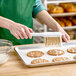 A person using an Ateco white pastry brush to put icing on a cookie.