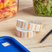 A roll of Noble Products Saturday Dissolvable Day of the Week labels next to a container of salad.