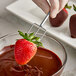 A person using an Ateco 3-prong dipping fork to dip a strawberry in chocolate.