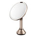 A simplehuman round rose gold stainless steel mirror on a metal stand with a light.