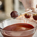 A person holding an Ateco stainless steel spiral dipping tool over a bowl of chocolate.