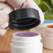 A hand holding a black 33/400 smooth plastic lid over a white container.