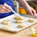 A person using an Ateco round pastry brush to brush dough on a baking sheet.