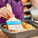 A person using an Ateco boar bristle brush to baste cinnamon rolls.