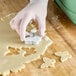 A person's hand with gloves using an Ateco butterfly cookie cutter to cut out cookies.