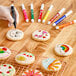 A hand using an Ateco food coloring marker to draw a rainbow on a cookie.