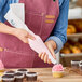 A person in a pink apron using an Ateco pastry bag to frost a cupcake.