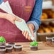 A person holding a green Ateco pastry bag over a cupcake with green frosting.