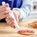 A hand using an Ateco Flex polyurethane-coated pastry bag to decorate a cookie.