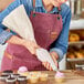 A woman in an apron using an Ateco pastry bag to decorate a cupcake with pink frosting.