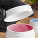 A hand in a black glove holding a 53/400 white lid on a white jar with pink liquid.