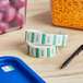 A blue tray on a counter with a roll of Noble Products Friday date labels next to a container of pasta.