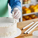 A person using an Ateco parchment-coated paperboard dowel to cut a cake.