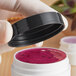 A hand holding a black 53/400 smooth lid on a jar of purple liquid.