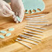 A gloved hand uses white plastic sticks from the Ateco Mini Sculpturing Tool Set to cut blue foam.