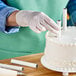 A hand in a white glove placing an Ateco parchment-coated paperboard dowel on a white cake.