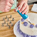 A person using an Ateco Decorating Syringe to pipe frosting on a cake.