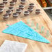 A cupcake with white frosting and brown piping on a cooling rack with pastry bags.