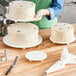 A person using an Ateco separator plate to make a white frosted cake with swirls on top.