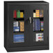 A black Tennsco storage cabinet with C-Thru doors holding books and files.