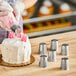 A person decorating a cake with a rose-shaped spiral of frosting using an Ateco tulip and rose piping tip.