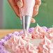 A hand using an Ateco star piping tip to pipe frosting on a cake.