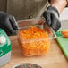 A person in gloves holding a container of shredded carrots made with an AvaMix Cadet 3/16" Grating / Shredding Disc.