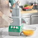 A person wearing gloves using an AvaMix Cadet continuous feed food processor to shred cheese in a professional kitchen.