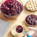 A hand using a spoon to add Lucky Leaf blackberry pie filling to a pie.