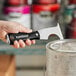 A hand holding a black and silver Allway Tools painter's multi-tool over a can of paint.