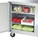 A Traulsen undercounter refrigerator with food inside, including tomatoes and meat.