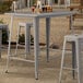 A Lancaster Table & Seating bar height outdoor table with drinks on it and stools around it.