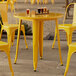 A Lancaster Table & Seating yellow metal table and chairs set up on an outdoor patio.