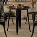 A Lancaster Table & Seating black metal outdoor table with black chairs on a patio.