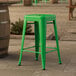 A Lancaster Table & Seating jade green outdoor counter height stool on a stone patio.