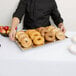 A man in a chef's uniform holding a Tablecraft stainless steel tray of bagels.