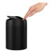 A hand reaching out to touch a black simplehuman countertop trash can.
