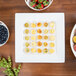 A 10 Strawberry Street Whittier white porcelain square platter on a table with blueberries, strawberries, and cheese.