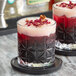 Two glasses with red and pink drinks garnished with cinnamon sticks and rose petals.