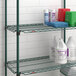 A Metroseal green Metro Super Erecta wire shelf holding white bottles of cleaning supplies.