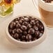 A bowl of Capora dark chocolate covered espresso beans next to a cup of coffee.