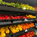 A black universal perforated metal shelf with yellow and orange bell peppers on it.